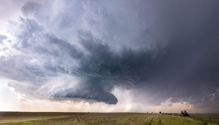 A massive supercell storm cloud forms in a funnel shape over the fields of Oklahoma.