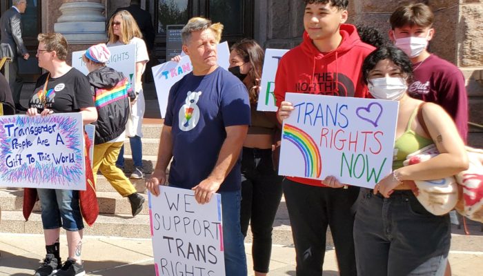 Activists gather at the Texas Capitol for a press conference in support of trans rights, holding signs which read "Trans Rights Now" "We Support Trans Rights" and "Transgender People Are A Gift To This World".